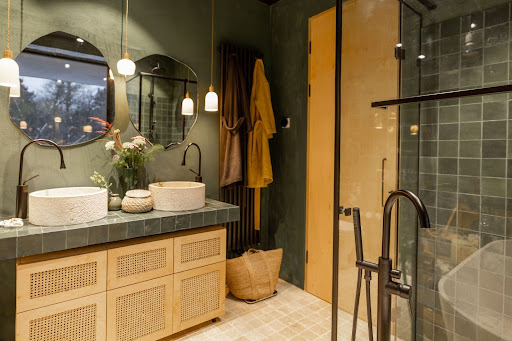 Modern bathroom with sage green walls, vessel sinks, wooden vanity, round mirrors, glass shower, and warm yellow accents.